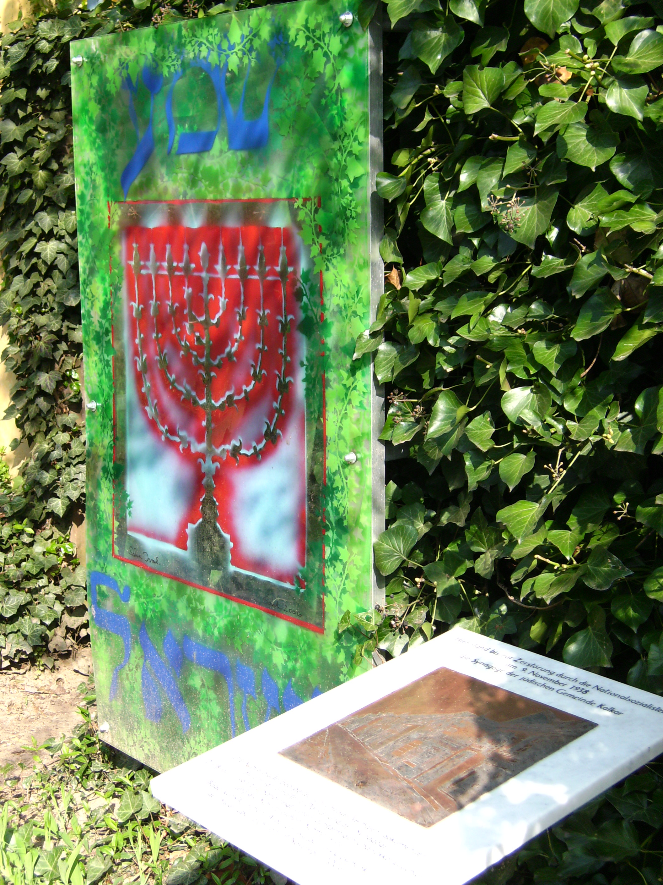 Das Bild zeigt eine Tafel mit einer Kupferplatte und einem farbigen Glasbild.