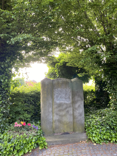 Thorarolle Kalkar Thorarolle, Denkmal aus grauem Stein mit hebräischer Inschrift umrahmt vom Grün von Bäumen und Hecken