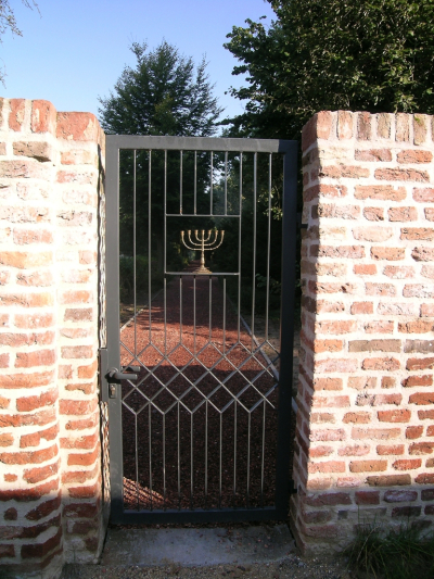 Eingangstor zum jüdischen Friedhof in Kalkar, Tor aus Eisenstäben mit einer Menora in der Mitte, eingelassen in eine Backsteinmauer 
