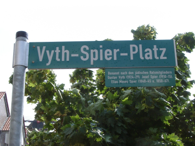Vyth-Spier-Platz in Kalkar Grünes Straßenschild mit der Aufschrift Vyth-Spier-Platz und einem Einschub mit Erläuterungen zur Namensgebung
