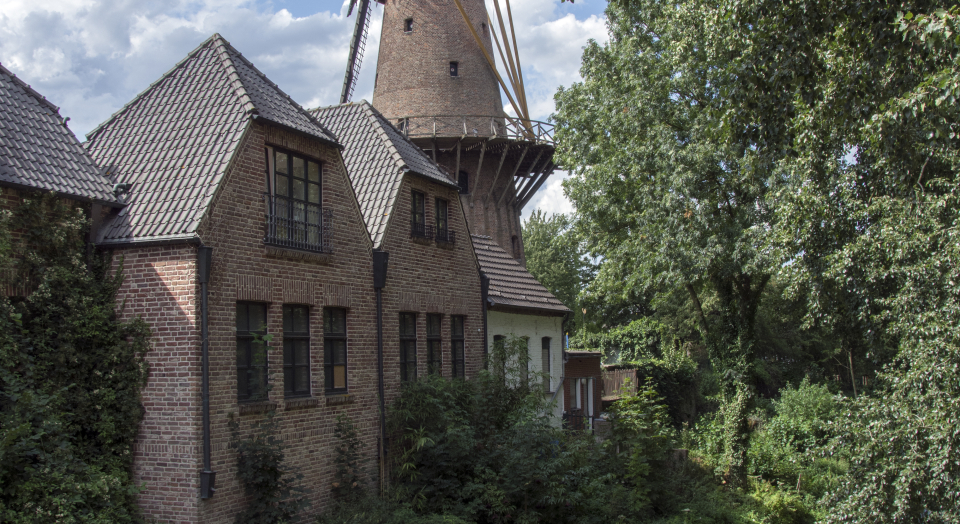 Blick über den Bach Ley mit grünen Uferböschungen und angrenzenden Bäumen auf die Kalkarer Mühle