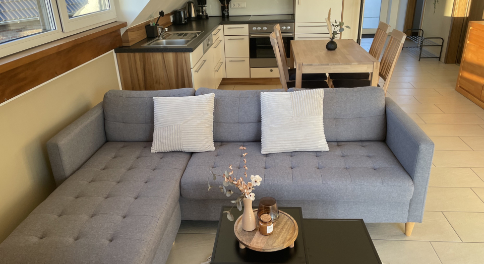 Ferienwohnung Am Pappelwäldchen, Sitzecke mit Tisch, im Hintergrund eine Küchenzeile mit Tisch und vier Stühlen