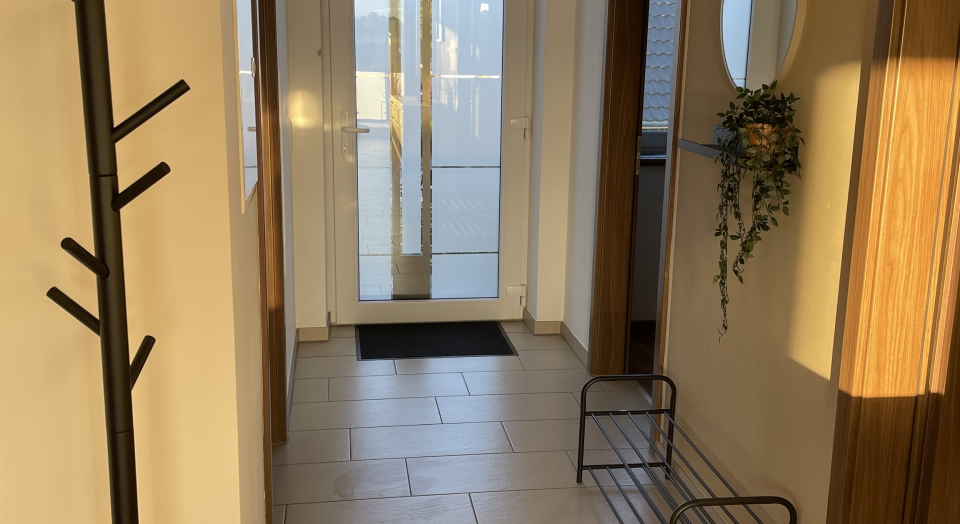 Ferienwohnung Am Pappelwäldchen, Blick durch den Flur mit Garderobe, Schuhregal und Spiegel auf die Eingangstüre 