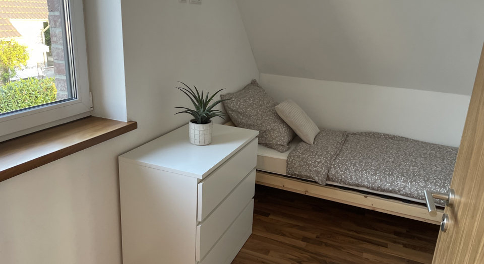 Ferienwohnung Am Pappelwäldchen, Blick auf ein Einzelbett mit Nachttisch unter einer Dachschräge