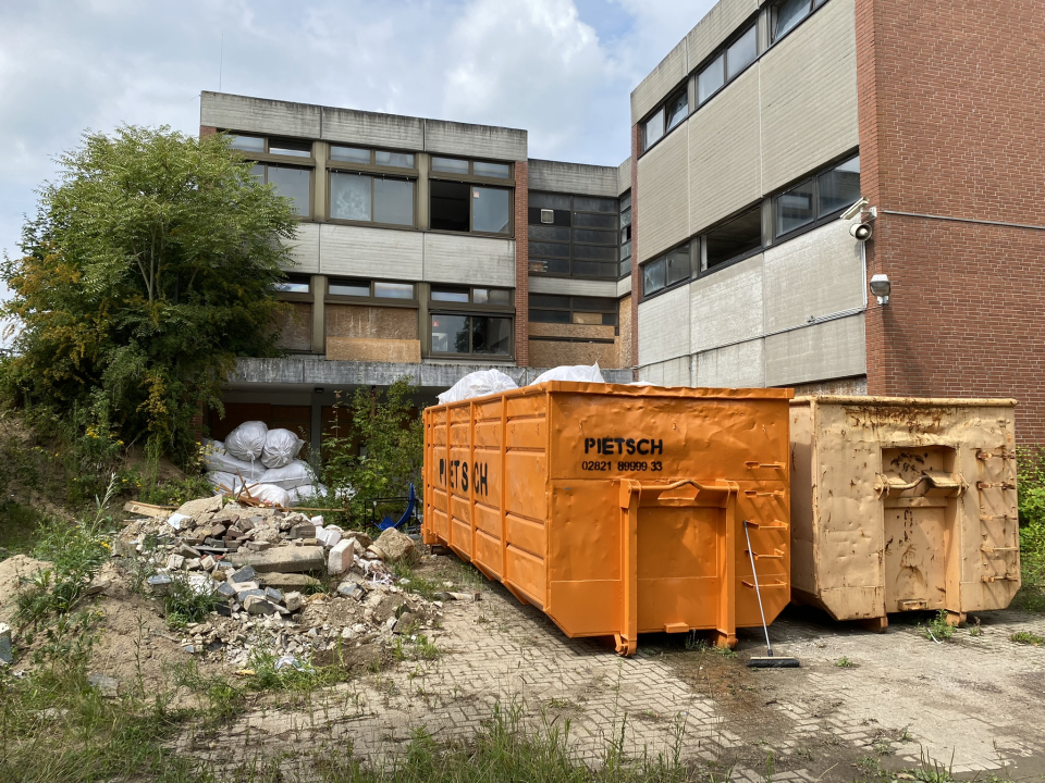 Blick auf Baucontainer vor dem Gebäudekomplex der alten Kalkarer Grundschule, die derzeit abgerissen wird.