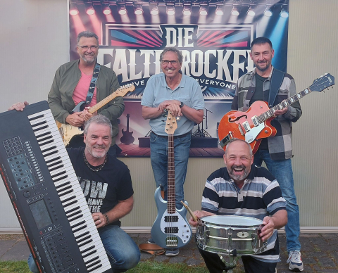 Mitglieder der Coverband mit ihren Musikinstrumenten vor einem Werbebanner der Band