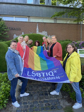 Das Foto zeigt die Gleichstellungsbeauftragten des Kreises Kleve und Vera van Oyen von „together“ mit einer Flagge zum Internationaler Tag gegen Homophobie (IDAHOBIT).