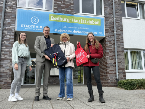 Übergabe der Staffeltasche mit Kalkarer Präsenten von der Kalkarer Bürgermeisterin Dr. Britta Schulz an Stephan Reinders, Bürgermeister von Bedburg-Hau vor dem Rathaus in Bedburg-Hau. Mit auf dem Foto: Kristin Voetmann, Tourismusbeauftragte der Gemeinde Bedburg-Hau und die Kalkarer Klimaschutzmanagerin Sabrina Meisen.